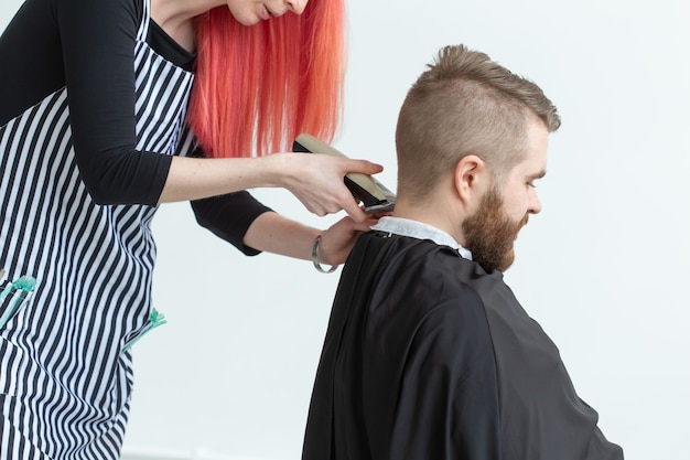 Concepto de peluquería, peluquería y peluquería - estilista mujer cortando a un hombre barbudo.