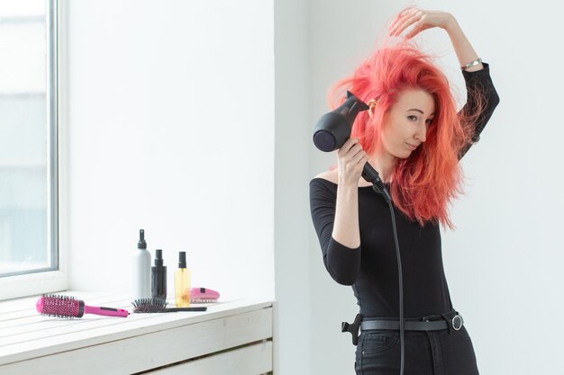 Concepto de peluquería, salón de belleza y personas - estilista de mujer joven con secador de pelo sobre fondo blanco.