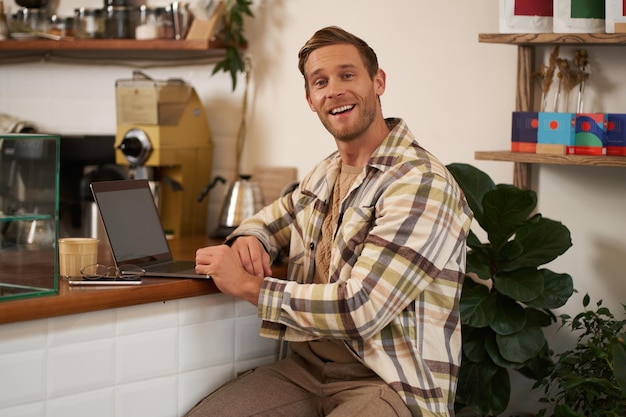 Foto concepto de pequeña empresa hombre de negocios guapo dueño de un café sentado cerca del mostrador con portátil y