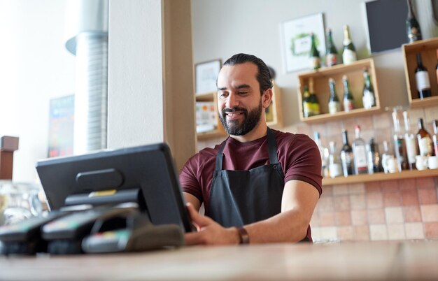 Foto concepto de pequeñas empresas, personas y servicios: hombre feliz o camarero en delantal en el mostrador con caja trabajando en el bar o cafetería