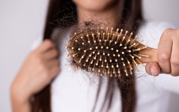 Concepto de pérdida de cabello y salud. Mujer sosteniendo un peine con su cabello dañado de larga caída.