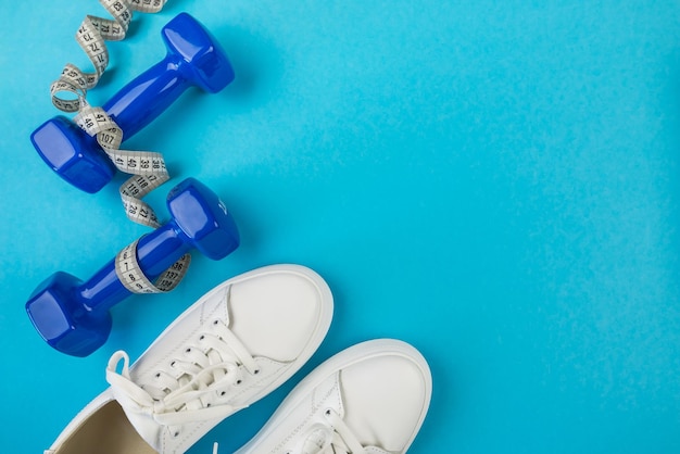 El concepto de pérdida de peso de deportes de fitness Foto de vista superior de zapatos deportivos blancos cinta métrica y mancuernas azules sobre fondo azul pastel aislado con espacio vacío Estilo de vida saludable