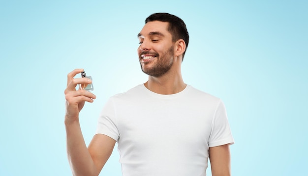 concepto de perfumería, belleza y personas - joven sonriente feliz con perfume masculino sobre fondo gris