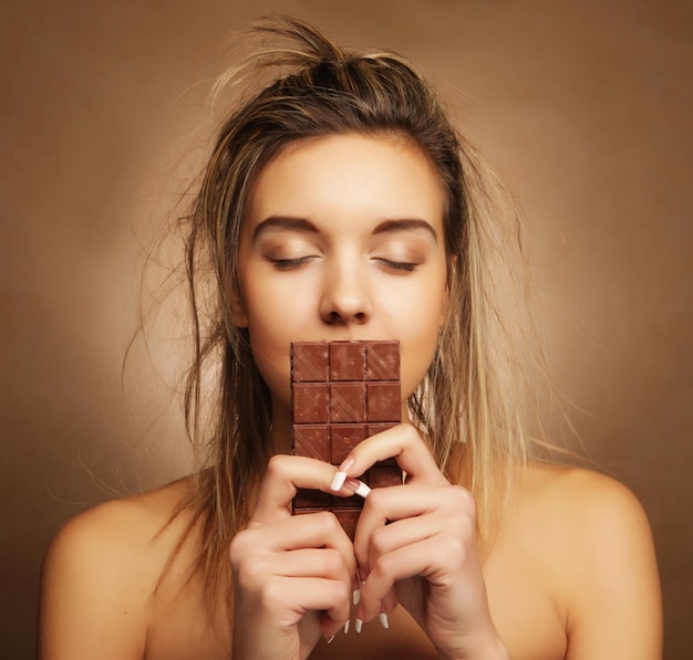 Concepto de personas y alimentos Hermosa chica rubia con chocolate sobre fondo beige