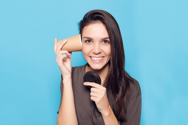 Concepto de personas, bebidas y estilo de vida - Mujer hermosa joven con café sobre fondo azul. Mujer atractiva feliz y sonriente. mujer con cabello oscuro sostiene un vaso de cartón con café