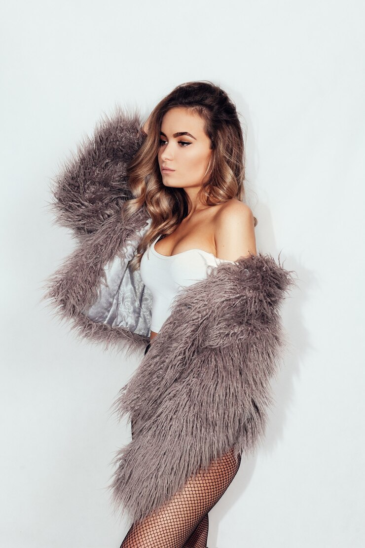 Foto concepto de personas, belleza y estilo de vida - joven hermosa morena con pelo rizado en un hermoso abrigo de piel y medias en la malla y ropa interior rosa sobre un fondo gris. estilo club.