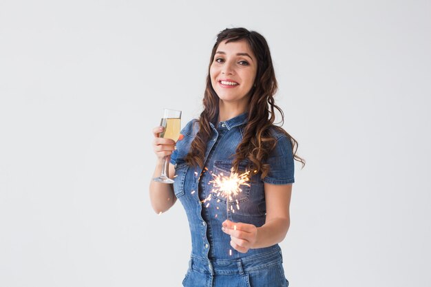 Concepto de personas, celebración y vacaciones - Mujer encantadora con bengala y copa de champán sobre fondo blanco con espacio de copia.