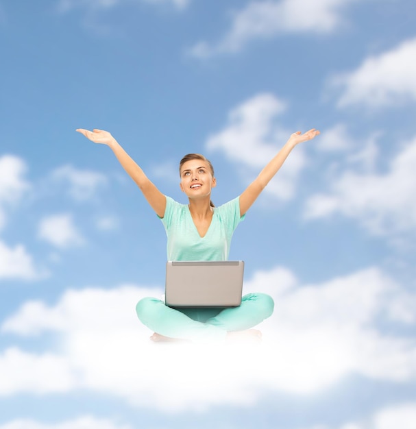 Foto concepto de personas, computación y tecnología - mujer joven feliz con computadora portátil sentada en la nube sobre fondo de cielo azul