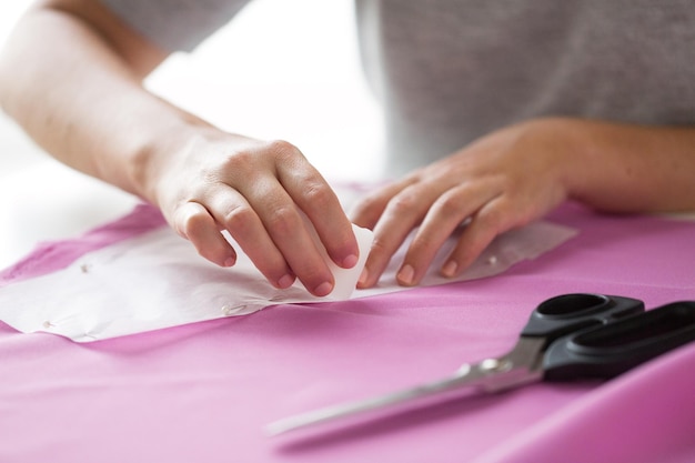 Foto concepto de personas, costura, costura y sastrería: mujer sastre con patrón de papel y dibujo de tiza sobre tela en el estudio de costura