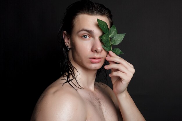 Concepto de personas, cuidado de la piel y belleza: joven mojado con cabello largo y negro sobre un fondo negro. Retrato masculino con pecho afeitado. Cuidado de la piel de los hombres. Hombre guapo musculoso rasgado sobre fondo negro