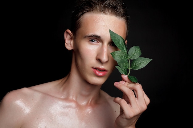 Concepto de personas, cuidado de la piel y belleza: joven mojado con cabello negro sobre fondo negro. Retrato masculino con el pecho afeitado. Cuidado de la piel de los hombres. Hombre guapo musculoso rasgado sobre fondo negro