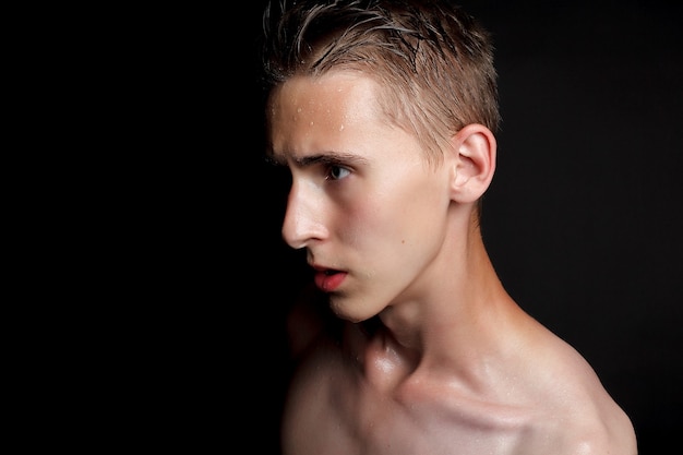 Concepto de personas, cuidado de la piel y belleza: joven mojado con cabello negro sobre fondo negro. Retrato masculino con pecho afeitado. Cuidado de la piel de los hombres. Hombre guapo musculoso rasgado sobre fondo negro