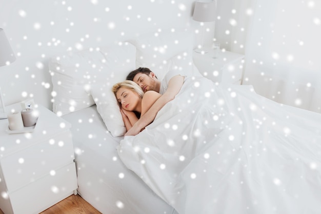 concepto de personas, descanso y relaciones - pareja feliz durmiendo en la cama en casa sobre la nieve