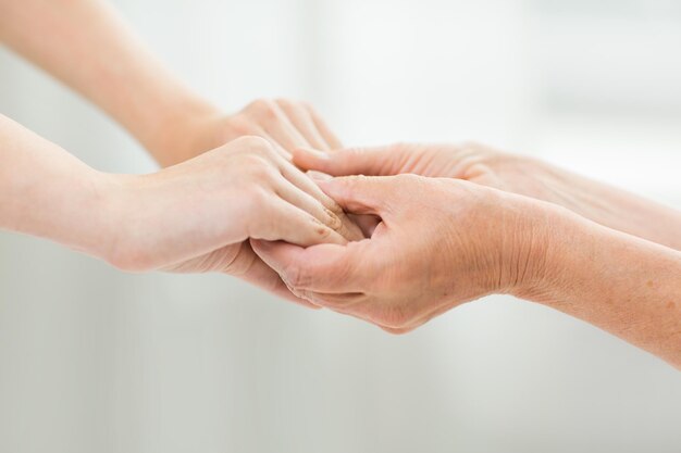 concepto de personas, edad, familia, cuidado y apoyo - cerca de una mujer mayor y una mujer joven tomándose de la mano