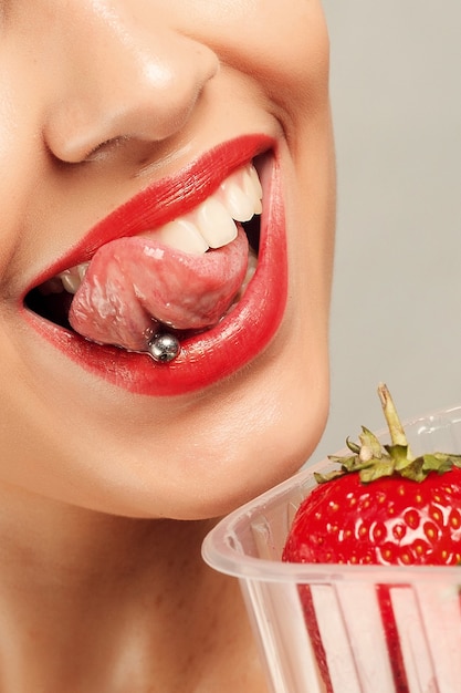 Concepto de personas, emociones, natural, comida, belleza y estilo de vida - Sexy Woman Eating Strawberry. Labios sensuales. Manicura y pintalabios. Deseo. Labios atractivos de la muchacha de la belleza con la fresa. dientes blancos