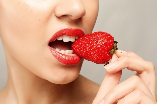 Concepto de personas, emociones, natural, comida, belleza y estilo de vida - Sexy Woman Eating Strawberry. Labios sensuales. Manicura y pintalabios. Deseo. Labios atractivos de la muchacha de la belleza con la fresa. dientes blancos