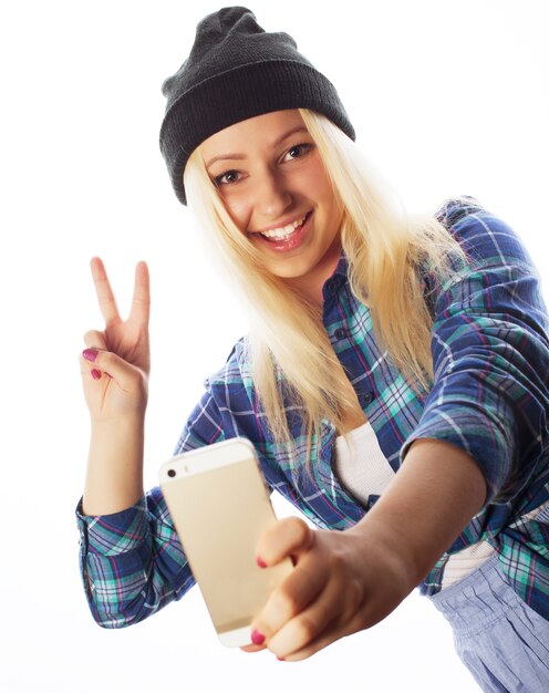 Concepto de personas, estilo de vida y tecnología: bonita adolescente con sombrero, tomando selfies con su teléfono inteligente, aislado en blanco