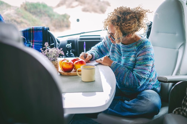 Concepto de personas de estilo de vida de vanlife de viaje Una mujer desayunando y escribiendo mapas de viaje por carretera sentada dentro de la cabina de una autocaravana moderna sola Señora viajera y concepto de libertad