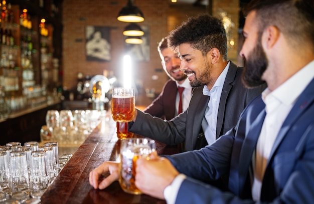 Concepto de personas, hombres, ocio, amistad y celebración. Amigos varones de negocios feliz bebiendo cerveza en el pub
