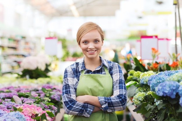 concepto de personas, jardinería y profesión - mujer feliz con flores en invernadero