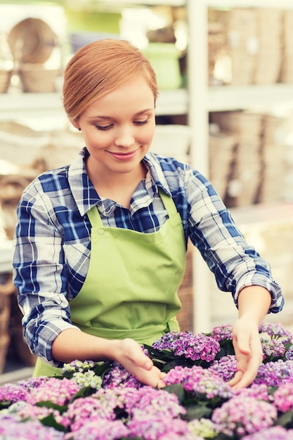 concepto de personas, jardinería y profesión - mujer feliz o jardinero cuidando flores en invernadero