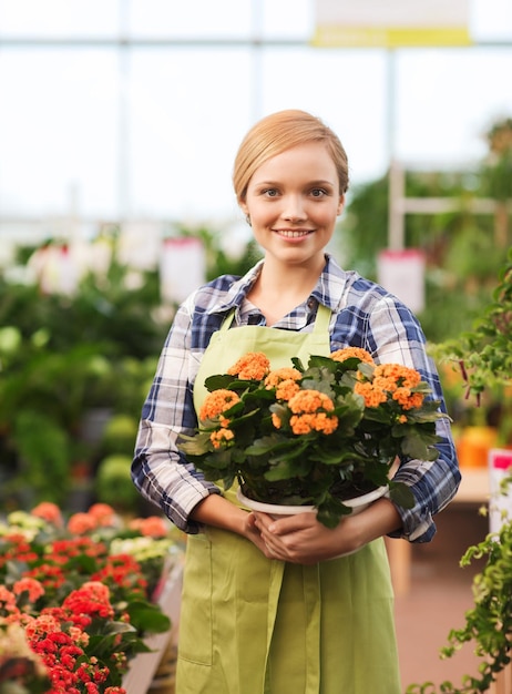 concepto de personas, jardinería y profesión - mujer feliz o jardinero sosteniendo flores en invernadero