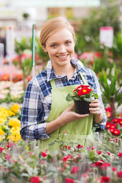 concepto de personas, jardinería y profesión - mujer feliz o jardinero sosteniendo flores en invernadero