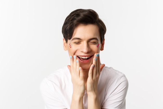 Concepto de personas, lgbtq y belleza. Primer plano de un hermoso hombre gay con uñas pulidas, riendo y mirando feliz, fondo blanco.