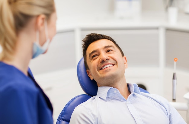 Foto concepto de personas, medicina, estomatología y atención de la salud - dentista femenina hablando con un paciente masculino feliz en la oficina de la clínica dental