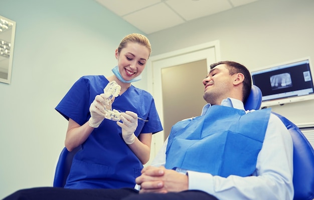 concepto de personas, medicina, estomatología y atención de la salud - feliz dentista masculino que muestra el diseño de la mandíbula a un paciente masculino en la oficina de la clínica dental