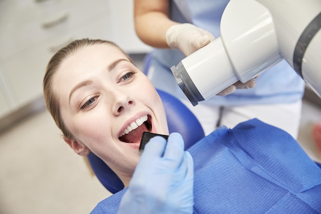 concepto de personas, medicina, estomatología, tecnología y atención de la salud: cierre del dentista que coloca un escudo intraoral en la boca de la paciente y asistente que dirige la máquina de rayos X en la clínica dental