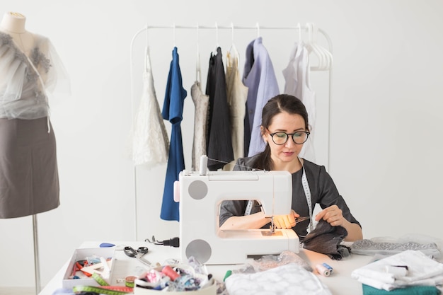 Concepto de personas y moda - mujer joven modista cose ropa en la máquina de coser.