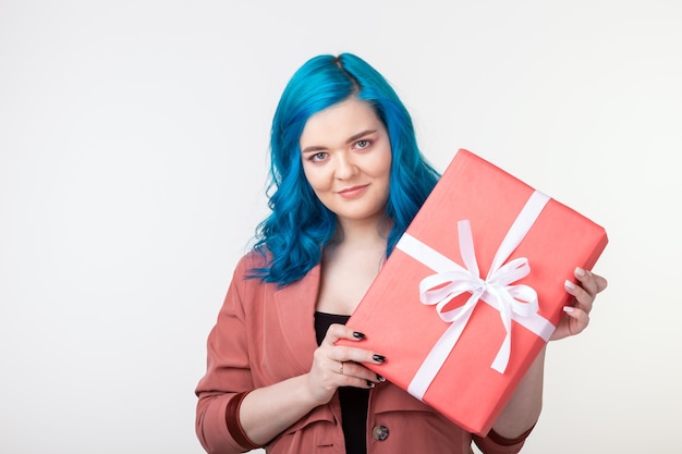 Concepto de personas, moda y vacaciones - hermosa chica con cabello azul de pie con caja de regalo sobre fondo blanco.