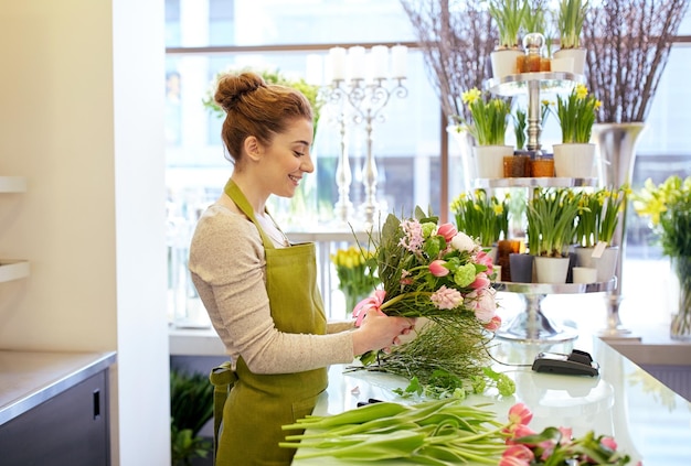 concepto de personas, negocios, venta y floristería - mujer florista sonriente feliz haciendo racimo en la floristería