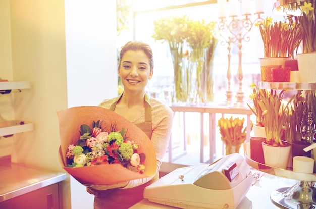 concepto de personas, negocios, venta y floristería - mujer florista sonriente feliz sosteniendo un ramo de flores envueltas en papel en la floristería