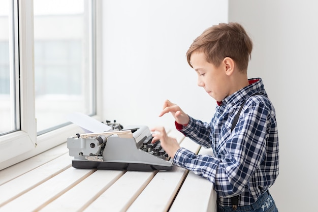 concepto de personas, niños y estilo - niño con vieja máquina de escribir negra sobre superficie blanca