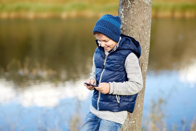 concepto de personas, niños y tecnología - adolescente feliz jugando o enviando mensajes de texto en un teléfono inteligente al aire libre