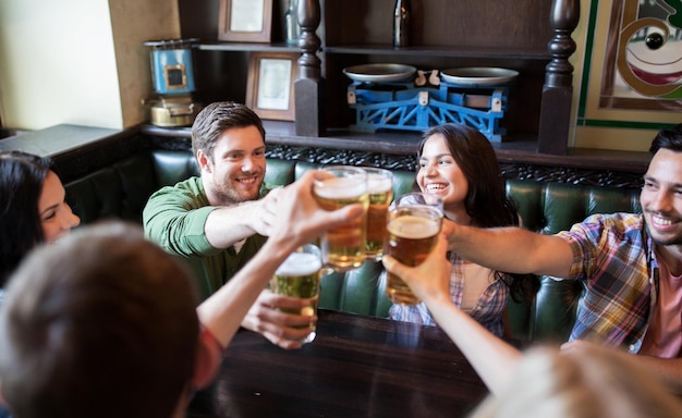 Foto concepto de personas, ocio, amistad y comunicación: amigos felices bebiendo cerveza, hablando y tintineando vasos en el bar o pub