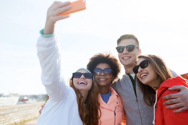 concepto de personas, ocio, amistad y tecnología - grupo de amigos adolescentes sonrientes tomando selfie con smartphone al aire libre