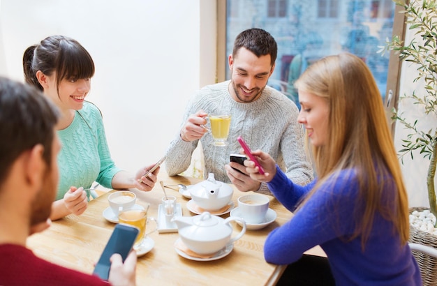 concepto de personas, ocio, amistad y tecnología - grupo de amigos felices con smartphones reunidos en un café y bebiendo té
