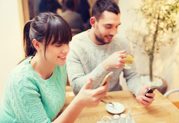 concepto de personas, ocio, amistad y tecnología - pareja sonriente con smartphones reuniéndose y bebiendo té en el café