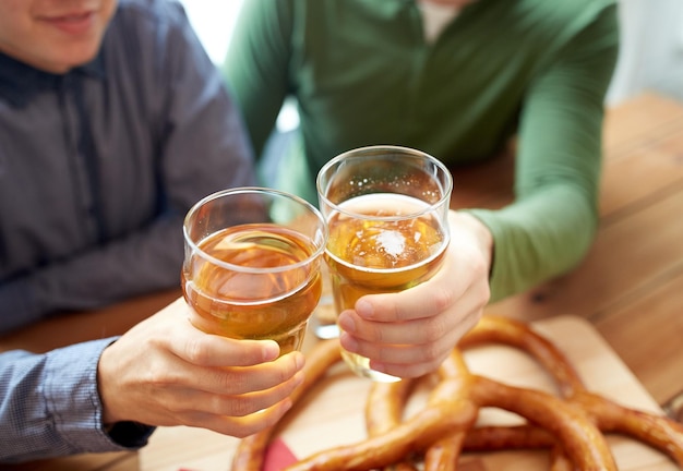 concepto de personas, ocio y bebidas - cierre de manos masculinas que tintinean vasos de cerveza y pretzels en el bar o pub