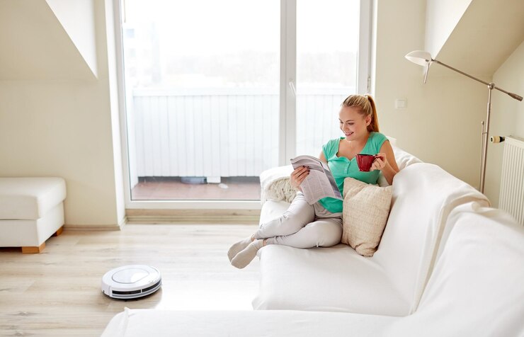 Foto concepto de personas, tareas domésticas y tecnología - mujer feliz leyendo revistas y bebiendo café mientras aspiradora robot en casa