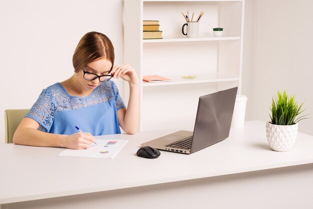 Concepto de personas, tecnología y educación - mujer joven estadounidense feliz sentada en la mesa con computadora portátil y libros en casa