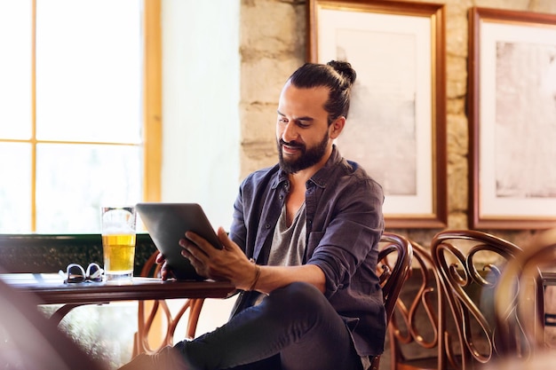 concepto de personas y tecnología - hombre feliz con tablet pc bebiendo cerveza en el bar o pub