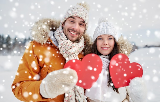 concepto de personas, temporada, amor y día de San Valentín - pareja feliz sosteniendo corazones rojos en blanco sobre el paisaje invernal