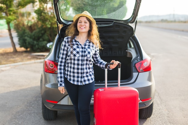 Concepto de personas, transporte y viajes: una mujer alegre está de pie cerca de su automóvil y está cerrando