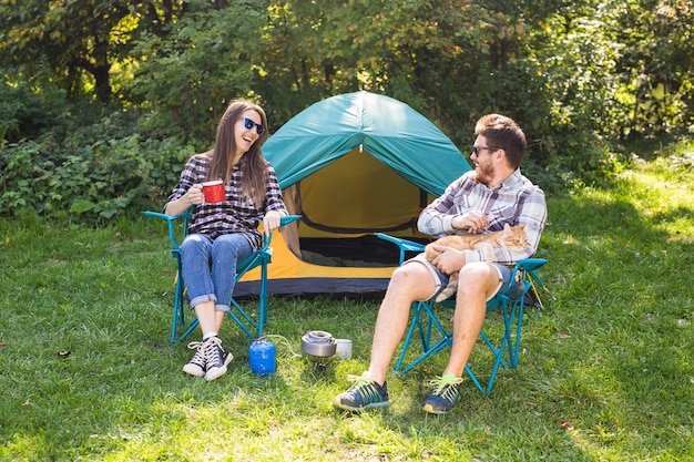 Concepto de personas, turismo y naturaleza: pareja divirtiéndose en un viaje de campamento y jugando con el gato