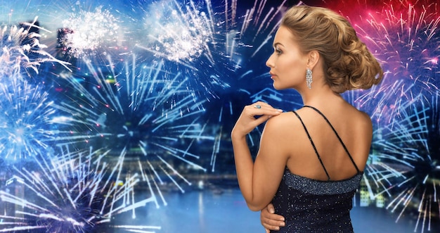 concepto de personas, vacaciones, fiestas, joyas y glamour - hermosa mujer con pendientes de diamantes sobre luces de fuegos artificiales en el fondo de la ciudad