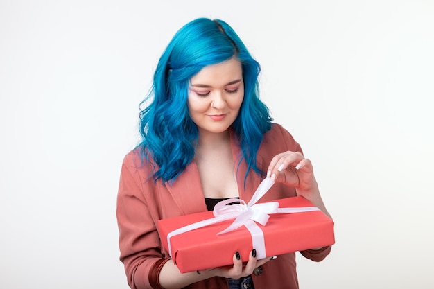 Concepto de personas, vacaciones y moda - Mujer joven feliz con cabello azul sosteniendo una caja de regalo sobre fondo blanco